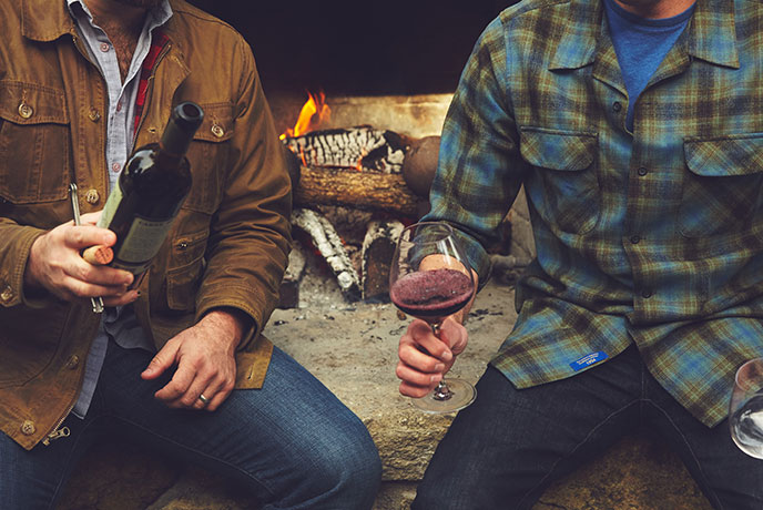 Rustic Carne lifestyle photo featuring Joe and friend sharing a bottle of wine in front of a fireplace