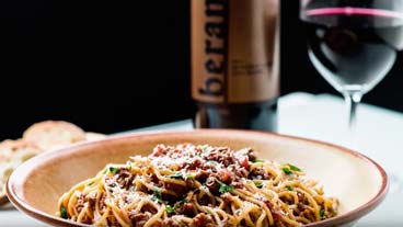 Beran wine bottle, glass of wine set behind a bowl of pasta bolognese